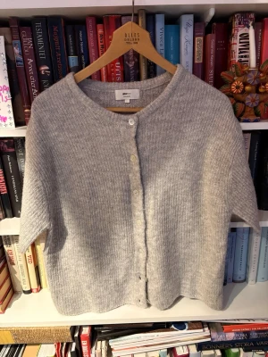 Ljusgrå kofta från Gina Tricot - Mysig ljusgrå kofta från Gina Tricot i ullblandning. Koftan har korta ärmar, rund halsringning och stängs med fyra vita knappar framtill. Perfekt för lager på lager och enkel att styla till olika outfits.
