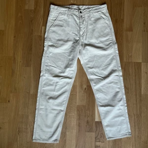 Beiga chinos från Lee - Snygga beiga chinos från Lee med raka ben och klassisk passform. Byxorna har framfickor, bälteshällor och stängs med knapp och dragkedja. Perfekta för en clean och avslappnad stil. Materialet känns mjukt och bekvämt, troligen bomull.