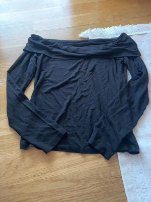 Svart offshoulder topp - Trendig svart offshoulder topp med långa ärmar och bred krage som vilar över axlarna. Perfekt för dig som vill ha en stilren och enkel look. Tillverkad i mjukt material som känns skönt mot huden.
