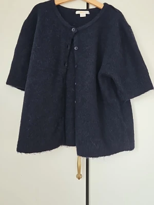 Mörkblå stickad kofta med knappar - Mysig mörkblå stickad kofta med korta ärmar och rund halsringning. Koftan har knappar framtill och en lite lösare passform. Ny utan prislapp