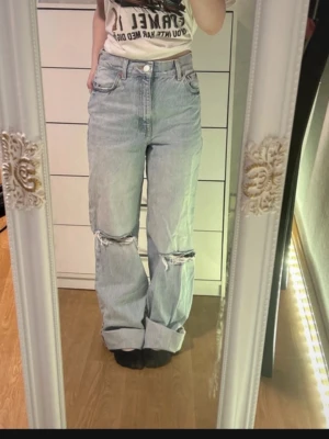 Jeans Zara 36 - Säljer ett par ljusblå baggy jeans med hög midja och fransade knän. Jag är 158cm och har vikt upp benen då de är för långa.