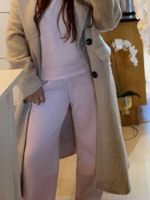 Lång beige teddyjacka med knappar - Säljer en lång och oversized teddyjacka i beige med dubbelknäppning och stora slag. Jackan har två fickor framtill och är tillverkad i ett mjukt, fluffigt material som ger en riktigt mysig känsla. Perfekt för kalla dagar och trendig look. Nypris 1200kr, använd ett par gånger, den är som ny.