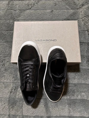 Svarta Vagabond sneakers i läder - Snygga svarta sneakers från Vagabond med ovandel i läder och vita, chunky sulor. Klassisk låg modell med svarta skosnören och stilren design. Vi frågor eller prisdiskution är det bara skriva! Skorna har bara varit använda en gång!