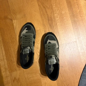 Valentino camo sneakers i grönt och svart - Snygga sneakers från Valentino med camomönster i grönt, svart och beige. Skorna har svarta detaljer, grov sula och klassisk snörning. Materialmix av mocka, textil och läder ger en exklusiv känsla. Perfekta för dig som vill sticka ut med stil.