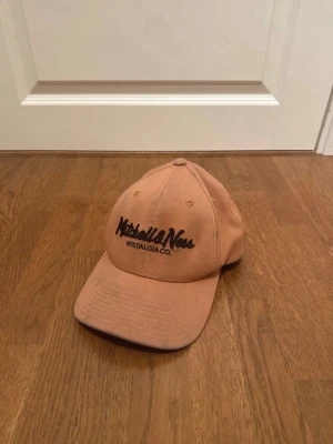 Orange keps från Mitchell & Ness - Säljer en beige keps från Mitchell & Ness med svart broderad logga framtill och texten 'Nostalgia Co.'. Klassisk böjd skärm och justerbar baksida. Tillverkad i bomullstyg som ger en avslappnad och stilren look. Med lite smuts på skärmen o lite uppe på kepsen, skriv om ni har frågor