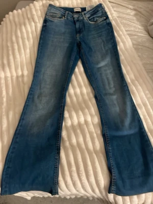 Blå bootcut jeans med slitningar - Säljer ett par blå bootcut jeans med snygga slitningar och klassisk femficksdesign. Jeansen har en ljusare tvätt framtill och vida ben. Perfekta för dig som gillar retrostil och vill ha ett par bekväma jeans i bomull.