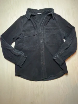 Svart manchester overshirt - Säljer en svart overshirt i manchester med klassisk krage och två stora bröstfickor med lock. Skjortan har långa ärmar med knapp vid manschetten och stängs med knappar framtill. Perfekt för lager på lager och en chill look.Ser lite annorlunda ut i ljuset😀diskutera pris gärna!