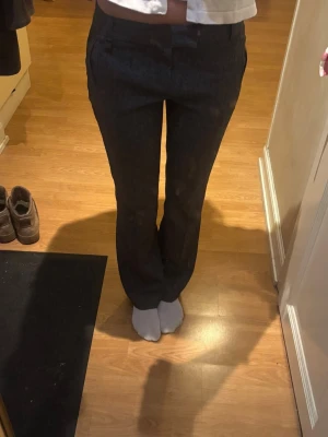 Mörkgrå kostymbyxor - Snygga mörkgrå kostymbyxor med raka ben och pressveck. Byxorna har hällor för skärp och diskreta fickor fram. Perfekta för en clean och stilren look. 