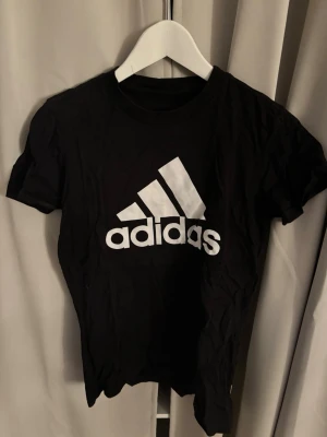 Svart Adidas t-shirt med logga - Snygg svart t-shirt från Adidas med stor vit logga på bröstet. rund hals och korta ärmar. I storlek S
