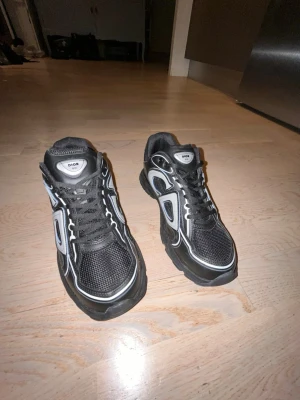 Svarta Dior sneakers med vita detaljer - Säljer ett par svarta Dior sneakers med vita och svarta detaljer. Skorna har en chunky sula, meshpaneler och reflekterande inslag. Klassisk snörning och låg profil gör dem perfekta för en trendig streetwear-look.och är helt nya