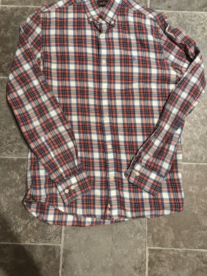 Rutig skjorta från Morris - Klassisk rutig skjorta från Morris i blått, rött och vitt. Skjortan har lång ärm, knappar framtill och en liten broderad logga på bröstet. Tillverkad i mjuk bomull och perfekt för en avslappnad men stilsäker look.