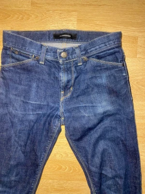 Blå slim fit jeans från J.Lindeberg - Snygga blå slim fit jeans från J.Lindeberg med klassisk femficksmodell och kontrastsömmar. Jeansen har normal midja och är tillverkade i ett slitstarkt denimtyg. Perfekta för dig som gillar en stilren och enkel look.