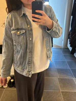 Klassisk ljusblå jeansjacka - Säljer en klassisk ljusblå jeansjacka med raka linjer och knappstängning framtill. Jackan har två bröstfickor med lock och knappar samt sidofickor. Tidlös modell som passar till det mesta och är enkel att styla. 