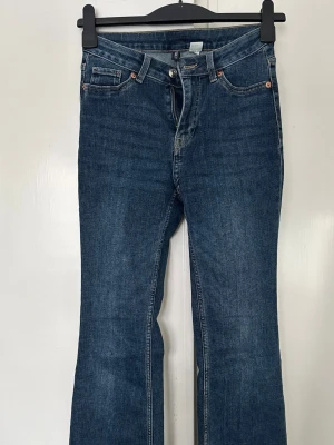 Mörkblå bootcut jeans - Säljer ett par mörkblå bootcut jeans med klassisk femficksdesign och knappgylf. Jeansen har en lätt utsvängd passform nedtill och är tillverkade i ett mjukt denimtyg. Perfekta för dig som gillar en retroinspirerad look.