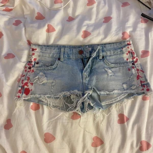 Lågmidjade korta jeansshorts - Snygga ljusblå jeansshorts från Gina Tricot med slitna detaljer, fransig kant och rosa färgstänk på sidorna. Korta och låg midja. Perfekta för sommaren och så snygga!!