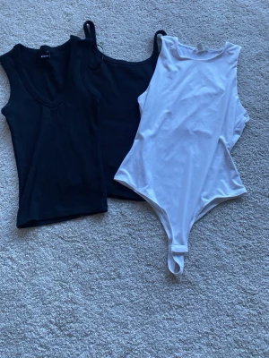 Svart och vit basic body set - Säljer ett set med två svarta linnebodys och en vit body. Alla har ärmlös design och rundad halsringning, den vita bodyn har knäppning i grenen. Perfekt att styla till olika outfits. Materialet känns mjukt och stretchigt.från H&M och Gina tricot 