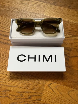 Gröna Chimi 04 - Snygga solglasögon med rektangulära bågar i brun transparent plast. Glasen är tonade och ger en cool retrovibe. Perfekta för dig som vill sticka ut med en trendig accessoar. Chimi 04. Nypris 1400. Skriv för fler bilder!