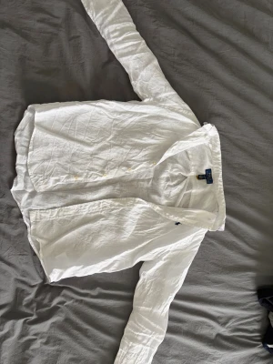 Vit linneskjorta från Ralph Lauren - Klassisk vit skjorta från Ralph Lauren i svalt linne. Skjortan har lång ärm, knappar framtill och den ikoniska broderade loggan på bröstet. Perfekt till jeans eller shorts för en clean och fräsch look.