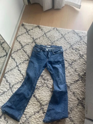 Blå bootcut jeans från Gina Tricot - Säljer ett par klassiska blå bootcut jeans från Gina Tricot. Jeansen har fem fickor, normal midja och är tillverkade i ett mjukt denimtyg. Perfekta för dig som gillar en avslappnad men ändå trendig look.