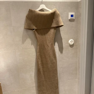 Adoore off shoulder klänning - Säljer en beige ribbad långklänning med bred offshoulder-krage. Klänningen har en figurnära passform och är tillverkad i ett stickat material som ger en mjuk och bekväm känsla. Perfekt för dig som gillar stilrena och trendiga plagg. Säljs inte längre på Adoore. Passar allt från 34-40, väldigt stretchig!