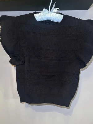 Svart pointelle-topp - Snygg svart pointelle-topp med korta ärmar och rund halsringning. Tröjan har ett diskret hålmönster och är gjord i ett mjukt stickat material. Perfekt för en trendig och avslappnad look. Stl. S (xs/s)