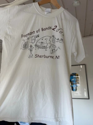Vit Pageant of Bands t-shirt - Vit t-shirt med tryck från Pageant of Bands 2000, Sherburne, NY. Framsidan har tecknade instrument och text, baksidan listar olika skolor.  vet inte mer om den då jag köpte den från Ettresex