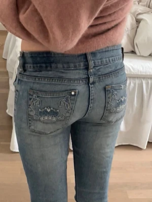 Bootcut jeans - Säljer ett par blå bootcut jeans med snygga broderade kronor på bakfickorna.💕De är köpta på second hand, och lappen finns kvar men är ganska suddig, det står typ ”& Ghio”. De är lite slitna i nedkanten, och har hål i grenen men det går att sy. Midjemått: 33 cm tvärs över Innerbenslängd: 74 cm 💗