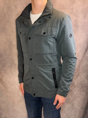 Grå/Grön J-Lindeberg Fieldjacket - Stl S - Riktigt snygg Fieldjacket från J-Lindeberg i färgen grå/grön! | Fint skick: 8/10, spår av användning och dragkedjan sitter lös men går att sätta på sig jackan | Stl: S, modellen är 177cm och väger 75kg, passar riktigt bra 🙌 | Hör av dig vid frågor // Galgen 🫡