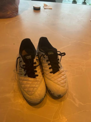 Nike Lunar Gato vita inomhus fotbollsskor, futsall - Säljer ett par vita Nike Lunar Gato fotbollsskor med svart swoosh och svarta snören. Skorna har quiltad ovandel i syntetmaterial och meshpaneler på sidorna för bra ventilation. Perfekta för futsal eller inomhusspel. Snygg och sportig design!