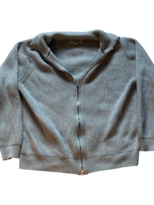 Grå mm6 ribbstickad ziptröja - Snygg grå ribbstickad tröja med dragkedja framtill och krage. Tröjan har långa ärmar och en avslappnad passform. Perfekt för lager på lager och enkel att matcha med olika outfits.