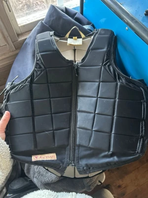 Svart säkerhetsväst från Racesafe  - Stl XL barn  Ok skick  Dragkedjan är trög och börjar nog ge upp, borde bytas snart därav pris men funkar idagsläget