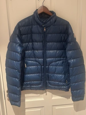 Ljusblå dunjacka från Moncler - En ljusare blå jacka från Moncler med storleken 4. Riktigt skön och håller värmen suveränt. Den perfekta och stiliga jackan inför våren.