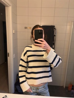 Vit stickad tröja med marinblå ränder - Säljer en vit stickad tröja med breda marinblå ränder. Tröjan har en boxig, rund halsringning och långa ärmar. Ribbstickade muddar vid ärmslut och nederkant. Hör av dig vid frågor💕