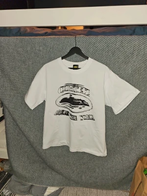 Corteiz Vit t-shirt med svart tryck - Vit t-shirt från Corteiz med ett stort svart grafiskt tryck på bröstet. Klassisk passform med rund hals och korta ärmar. Perfekt för dig som gillar enkel men cool streetwear-stil. Är öppen för prisförslag vid snabb försäljning. Är öppen för prisförslag vid snabb försäljning.