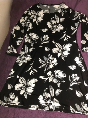 Svart blommig klänning från SHEIN - Svart klänning från SHEIN med stora vita blommor. Klänningen har lång ärm, rund halsringning och en lätt utställd passform. Perfekt för dig som gillar en stilren men ändå iögonfallande look.