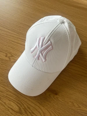  New Era keps - Snygg vit - krämvit keps från New Era med klassisk New York Yankees-logga broderad i ljusrosa framtill. Kepsen har böjd skärm och justerbar rem bak. Har några svaga missfärgningar men är i övrigt bra skick 🩷