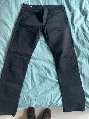 Svarta raka jeans från Jack & Jones - Säljer ett par svarta jeans från Jack & Jones med rak passform och klassisk femficksdesign. Jeansen har normal midja och är tillverkade i ett slitstarkt denimtyg. Knappgylf. Perfekta för dig som gillar en enkel och stilren look.