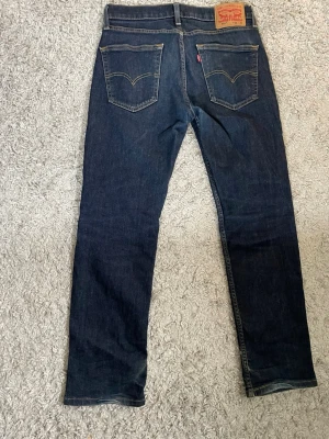 Mörkblå Levi's jeans W30 L30 - Säljer ett par klassiska mörkblå jeans från Levi's , och två bakfickor med den ikoniska sömmen. Jeansen har en läderpatch bak i midjan och Levi's röda etikett på fickan. Perfekta för en avslappnad och tidlös stil. St W30 L30