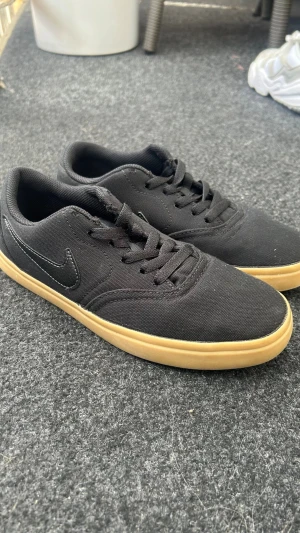 Svarta Nike sneakers med gummisula - Säljer ett par svarta Nike sneakers med klassisk låg profil och svart swoosh på sidan. Ovandelen är i textil och sulan är i ljusbrunt gummi för en clean kontrast. Skorna har svarta skosnören och passar perfekt till streetwear och casual outfits.