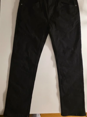 Svarta raka jeans från 157 - Säljer ett par svarta jeans från 157 med rak passform. Klassisk femficksmodell och normal midja. Jeansen är tillverkade i ett slitstarkt bomullstyg och har metallknappar och nitar. Perfekta för en clean och enkel stil      Midja: 45 cm  Benlängd: 77 cm  Hela: 106 cm