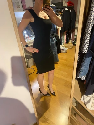 Svart tight ärmlös klänning - Snygg svart tight klänning med ärmlös design och rundad halsringning. Klänningen har en klassisk, enkel siluett som framhäver figuren och slutar strax ovanför knäna. 