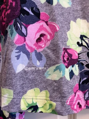 Grå sweatshirt med blommigt tryck Carven - Supersnygg grå sweatshirt från Carven med stora färgglada blommor i rosa, lila, limegrönt och blått. Tröjan har rund halsringning och långa ärmar. Perfekt för dig som vill sticka ut med ett unikt blommönster och mjukt material.Har en mjuk insida.Har tyvärr tagit bort lappen i nacken.