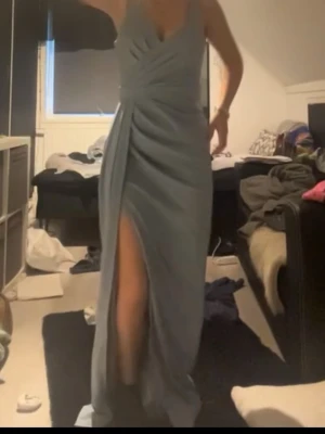 Ljusblå långklänning med slits - Elegant ljusblå långklänning med djup slits framtill och draperade detaljer över bysten. Klänningen har smala axelband och en figurnära passform som framhäver siluetten. Perfekt för speciella tillfällen. Skriv för mer bilder