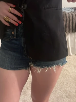 Mörkblå jeansshorts med rå kant - Snygga mörkblå jeansshorts med fransig, rå kant och klassisk femficksdesign. Shortsen har en högmidjig passform. Använt fåtal gånger. 