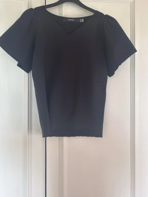 Svart v-ringad topp från Vero Moda - En svart topp från Vero Moda med v-ringning och korta, lite puffiga ärmar. Enkel och stilren design som passar till det mesta. Tillverkad i ett mjukt material som känns bekvämt mot huden.