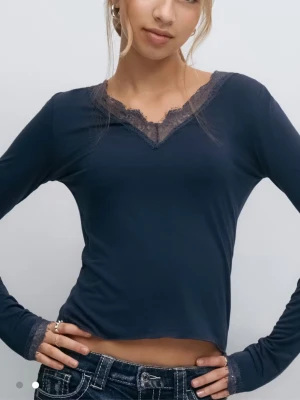 Mörkblå långärmad topp med spets - Mörkblå långärmad topp med v-ringning och spetsdetaljer vid halsringningen och ärmsluten. Tunn och mjuk kvalitet som sitter tight mot kroppen. Perfekt att styla med jeans eller kjol för en trendig look.