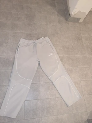 Grå mjukisbyxor från North Face - Säljer ett par grå mjukisbyxor från The North Face med vita kontrastsömmar och dragsko i midjan. Byxorna har raka ben, två sidofickor och logga broderad på vänster lår. Perfekta för chill dagar eller när du vill ha en clean streetwear-look.