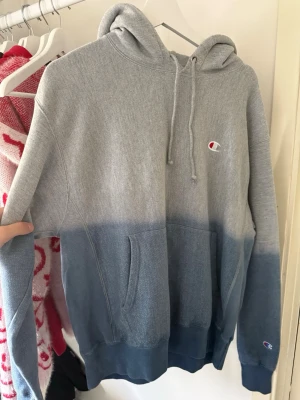Champion hoodie i grå och blå dip dye - Säljer en snygg hoodie från Champion i grått och blått dip dye. Klassisk huva med dragsnören, magficka och liten Champion-logga på bröstet och ärmen. Perfekt för dig som gillar streetwear och vill ha en chill look.