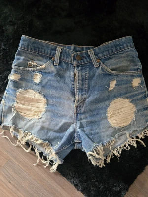 Levis vintage slitna jeansshorts med fransar - Säljer ett par blå jeansshorts med stora slitningar och fransig kant från levis. Perfekta för en avslappnad och trendig sommarlook. Riktigt fint skick