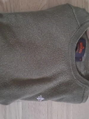 Olivgrön tröja Morris - Snygg olivgrön tröja från Morris med rund halsringning och diskret broderad logga på bröstet. Tröjan har långa ärmar och ribbade muddar vid ärmslut och nederkant. Perfekt för en stilren och avslappnad look.